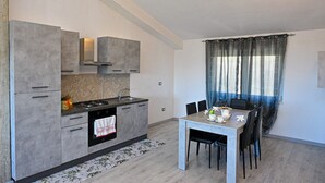 A modern kitchen with grey cabinets, a stove, and a dining area with a table and chairs. - Villa Donato (Filiano)