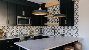 Cocina moderna con armarios oscuros, una isla grande, electrodomésticos de acero inoxidable y un salpicadero con estampado geométrico.