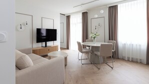 A modern living room with a flat-screen TV, a beige sofa, a dining table with chairs, and a large window with curtains. - Native Apartments Prądnicka 48 (Kraków)