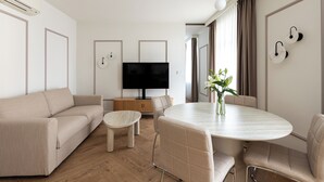 A modern living room with a sofa, a TV, a dining table, and chairs. - Native Apartments Prądnicka 48 (Kraków)
