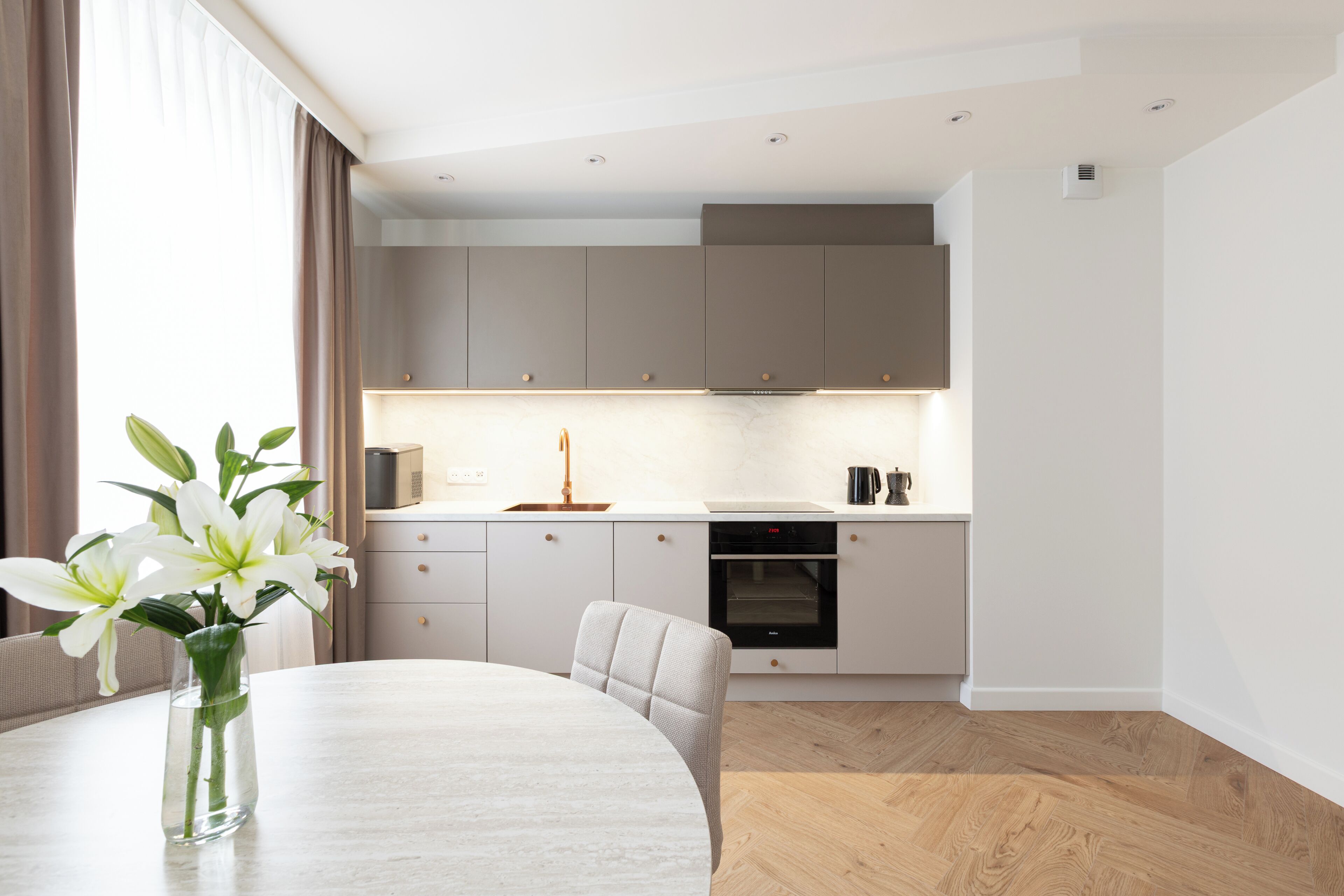 A modern kitchen with a built-in oven, a dining table with chairs, and a vase with flowers on the table.