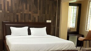 A modern bedroom with a large bed, a wooden headboard, a small desk, and a chair. - Coromandel Suites (Chennai)