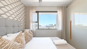 Ein modernes Hotelzimmer mit einem großen Bett, Blick auf die Stadt durch das Fenster und einer Wand mit Muster.