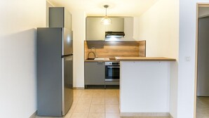 A compact kitchen with a built-in oven, a refrigerator, and a wooden countertop.
