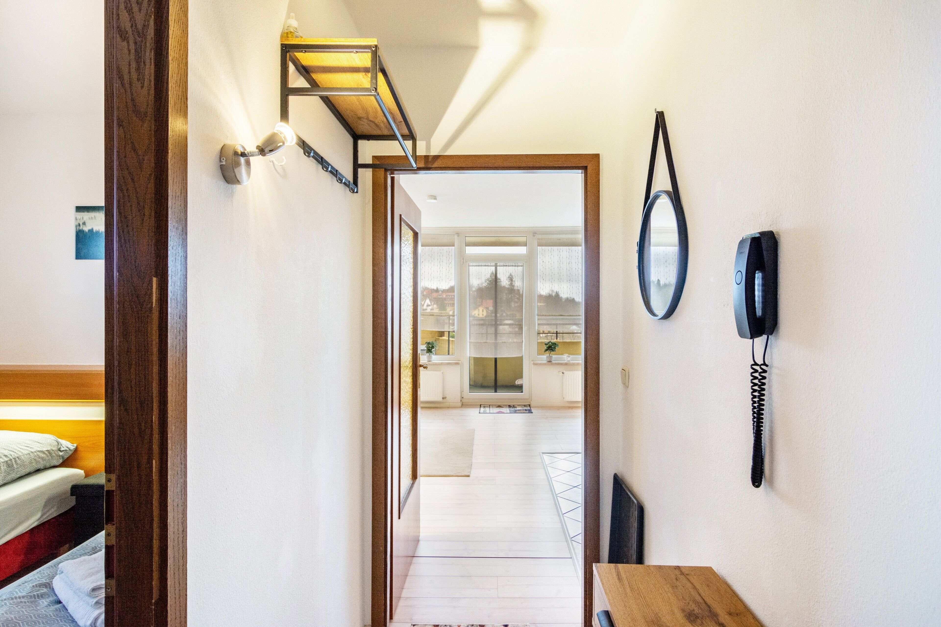 Un couloir avec une porte en bois, un téléphone fixé au mur et un miroir.