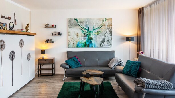 Een moderne woonkamer met een grijze bank, een salontafel, een bijzettafeltje en een schilderij van een hert.
