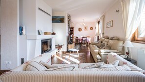 Ein Wohnzimmer mit Kamin, Sofa, Esstisch und Blick ins Freie.