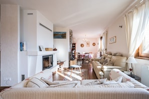 Ein Wohnzimmer mit Kamin, Sofa, Esstisch und Blick ins Freie.