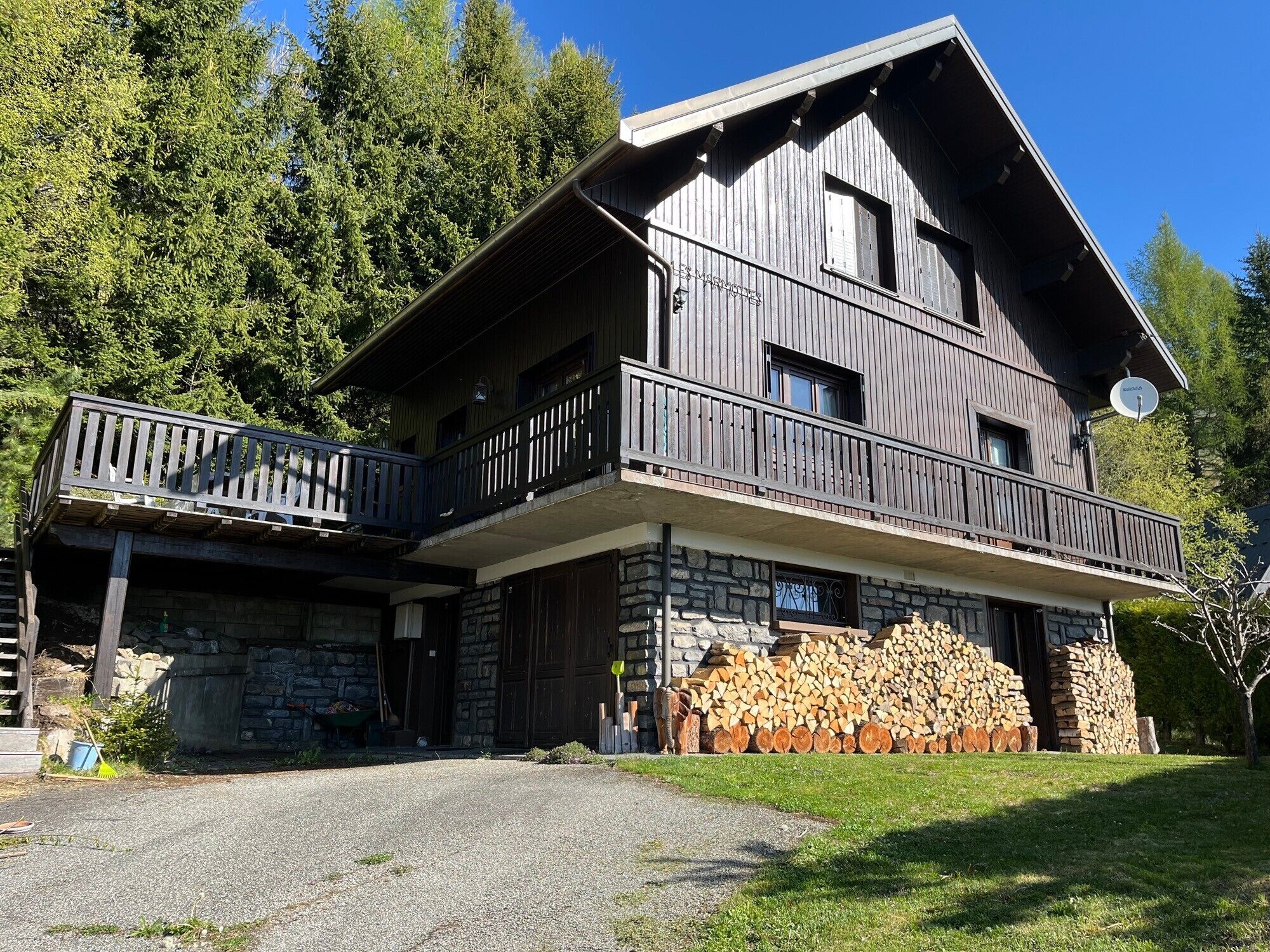 A two-story wooden house with a stone foundation, a balcony, and a satellite dish.