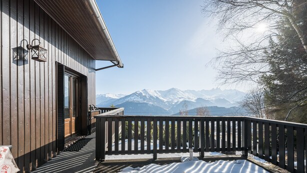 Ein Holzbauten mit Balkon, Tür und Blick auf schneebedeckte Berge.