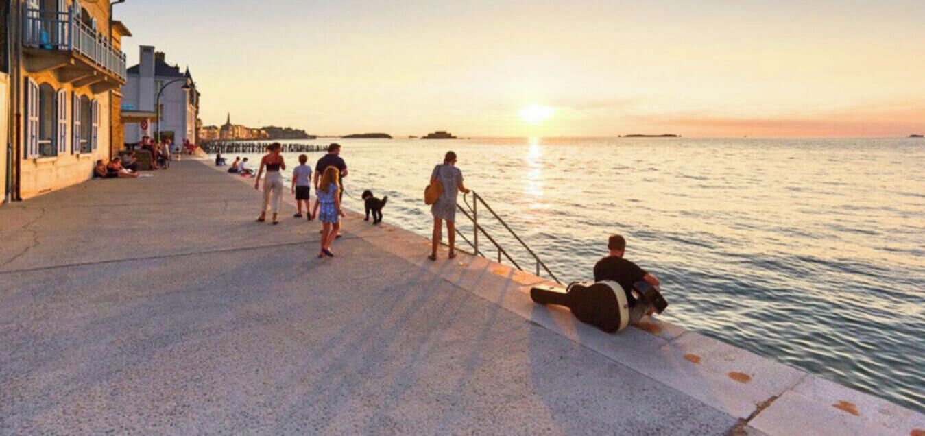 Um calçadão à beira-mar com pessoas caminhando e sentadas, com vista para o oceano.