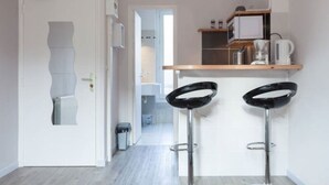 Une cuisine moderne avec deux tabourets de bar noirs, une porte blanche et une vue sur la pièce adjacente.