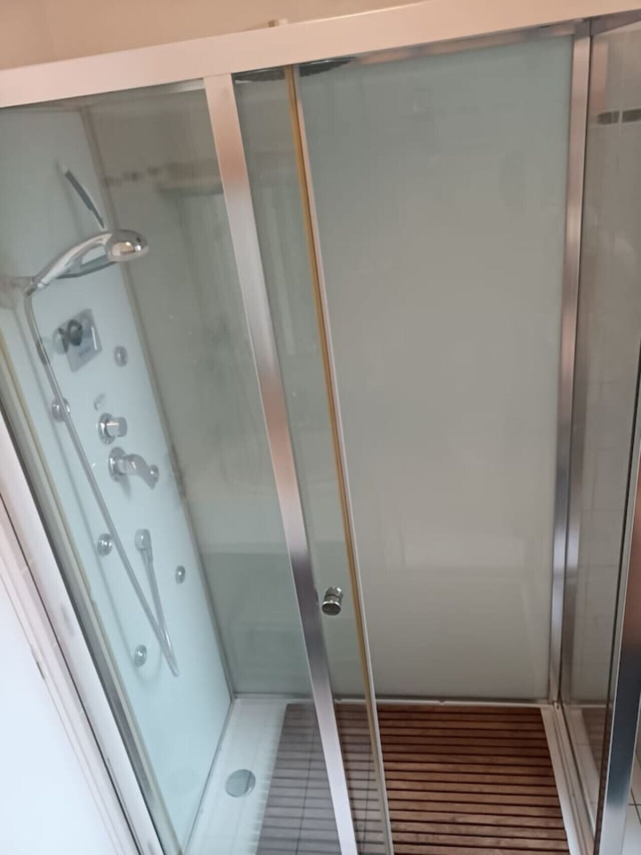 A glass-enclosed shower stall with a handheld showerhead, a wall-mounted faucet, and a control panel.