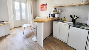 Kompakti keittiö, jossa on puinen työtaso, valkoiset kaapit ja ikkuna, jossa on verhot.