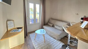 Kompakti hotellihuone, jossa on sohva, pieni pöytä, työpöytä ja ikkuna, jossa on verhot.
