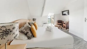 A modern bedroom with a large bed, a bedside table, a lamp, and a view of the outside. - Bord de l`eau 1 - T3 - Vue mer (Cancale)