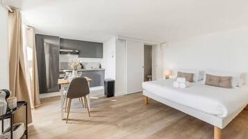 Ein modernes Schlafzimmer mit einem großen Bett, einer Essecke mit Tisch und Stühlen sowie einer Küchenzeile mit Schränken und Geräten.
