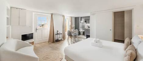Ein modernes Hotelzimmer mit einem großen Bett, einer Sitzecke mit einem Sessel, einem kleinen Schreibtisch und Blick auf die Stadt.