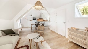 A modern loft apartment with a high ceiling, exposed wooden beams, a dining area, and a cozy seating space. - Parking privé - Au bord de l`eau 6 (Cancale)