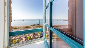 A view from a window overlooking a beach with a clear sky, a calm sea, and a promenade with umbrellas. - Parking privé - Au bord de l`eau 6 (Cancale)
