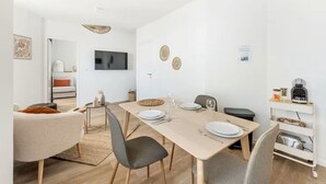 Ein moderner, gut beleuchteter Essbereich mit einem langen Tisch, gedeckt für vier Personen, umgeben von Stühlen. Ein Flachbildfernseher ist an der Wand oberhalb des Tisches angebracht.