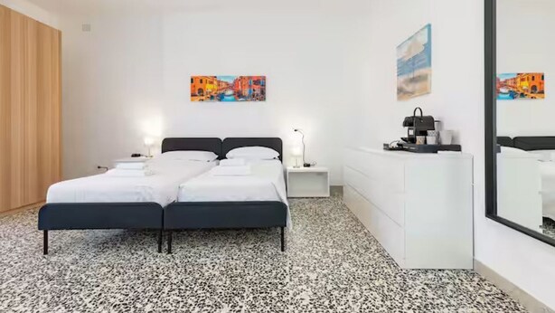 A bedroom with a bed, bedside tables, a dresser, and wall art. - Private room in Mestre with direct bus to Venice (ve)