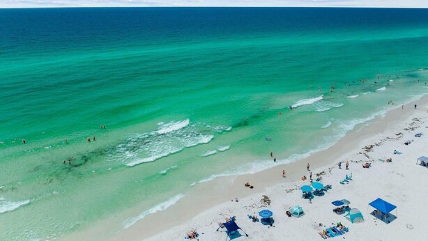 A beach with clear turquoise waters, a sandy shore, and several beach umbrellas and chairs. - Destin to Relax (Destin)