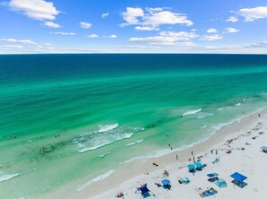 A beach with clear turquoise waters, a sandy shore, and several beach umbrellas and chairs. - Destin to Relax (Destin)