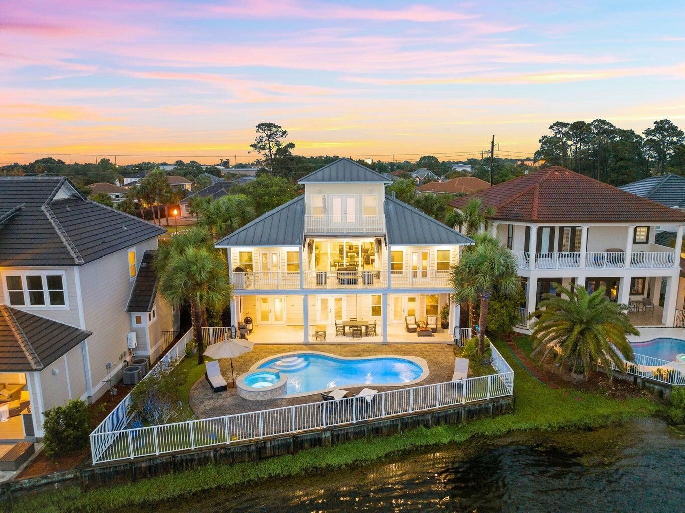 A large two-story house with a swimming pool, surrounded by a fence and palm trees.