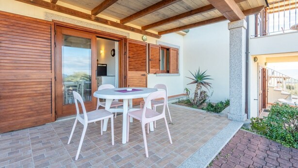 Une terrasse avec une table ronde et des chaises, des volets en bois et un sol carrelé.