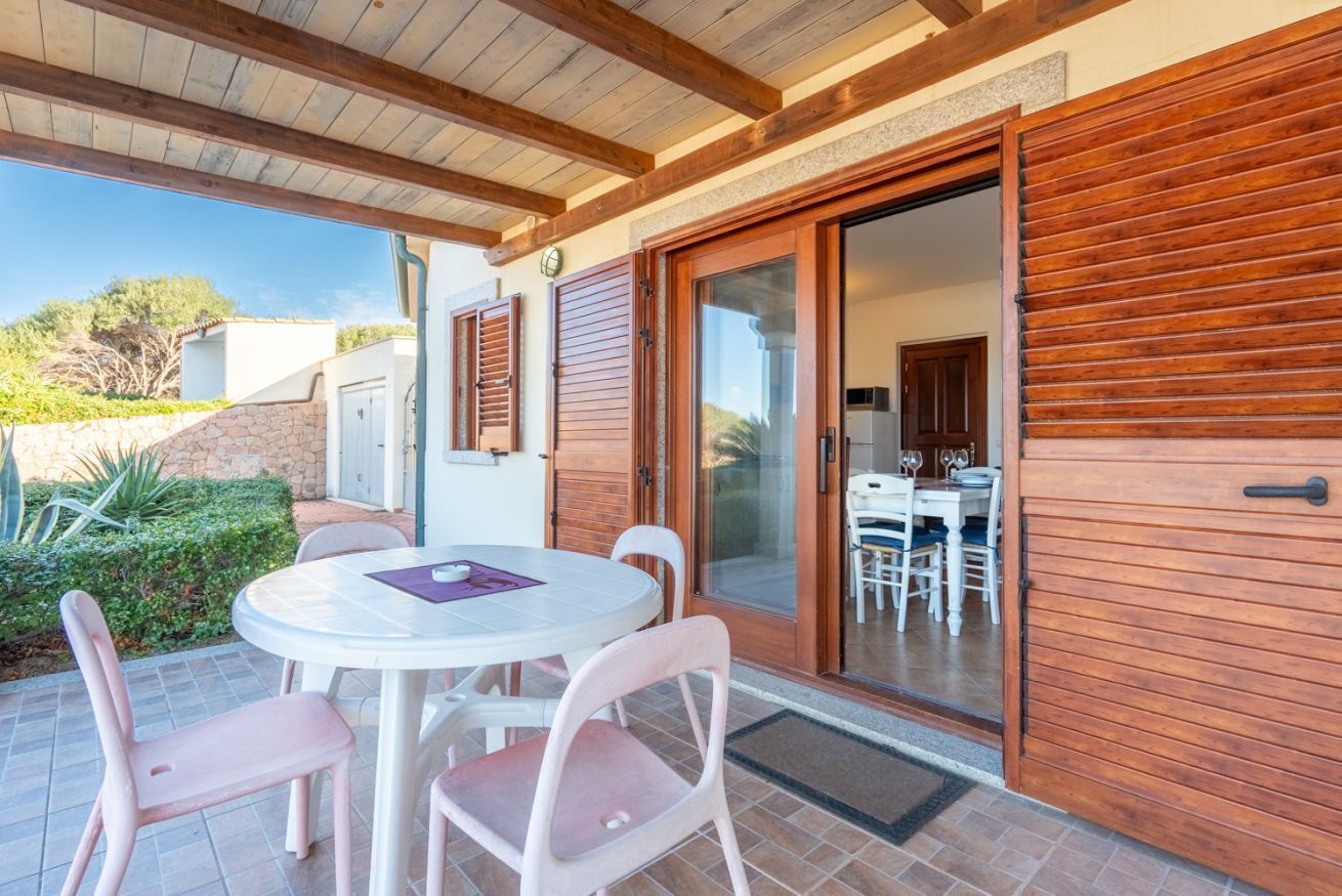 Eine Terrassengruppe im Freien mit rundem Tisch und Stühlen, ein hölzerner Pergola darüber und eine Glasschiebetür zu einem Innenbereich mit Essplatz.