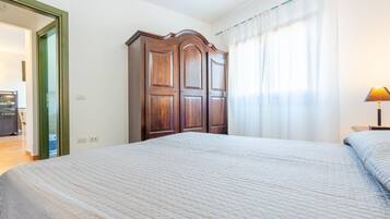 A bedroom with a large bed, a wooden wardrobe, and a window with sheer curtains.