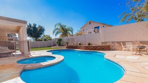 Una piscina con cubierta de piedra, rodeada por un muro de ladrillo y una zona de estar techada con sillas.