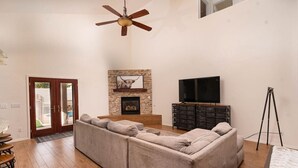 Amplia sala de estar con un sofá modular, una chimenea, un televisor montado y un ventilador de techo.
