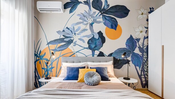 Een slaapkamer met een bed, hoofdbord, nachtkastje en een muur met een bloemenmuur.
