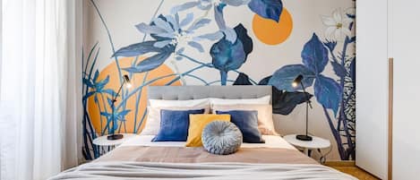 A bedroom with a bed, a headboard, a bedside table, and a wall with a floral mural.