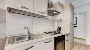 Een moderne keuken met een RVS spoelbak, een gasfornuis en houten kastjes.