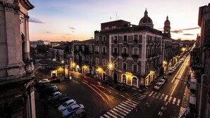 A historic building with classical architecture, a wide street, and parked cars. - To complete (Catania)