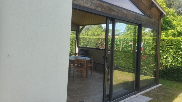 Un porche cubierto con mesa y sillas, una parrilla y vistas a un jardín.