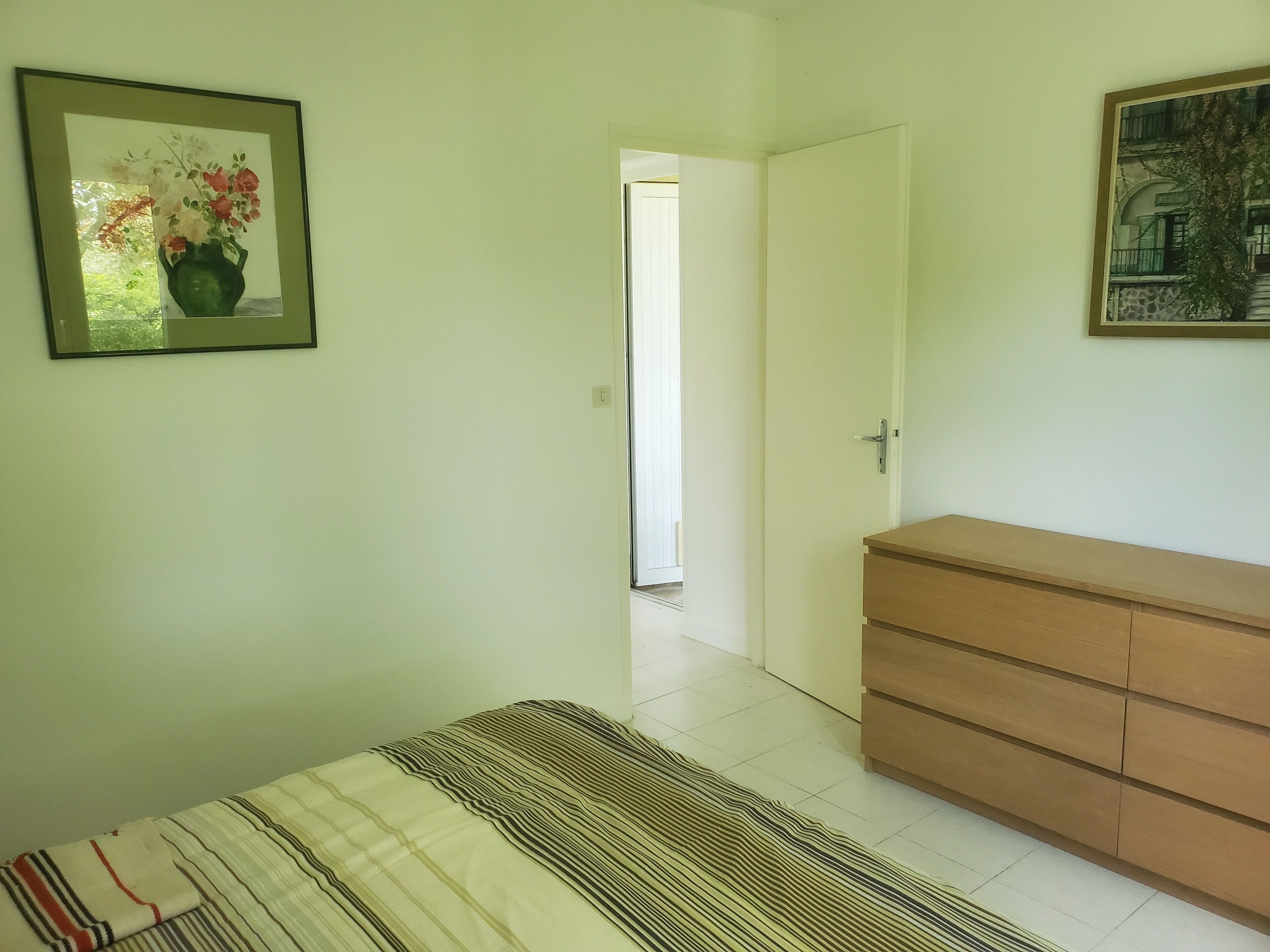 Een slaapkamer met een bed, een dressoir en een deur naar een andere kamer.