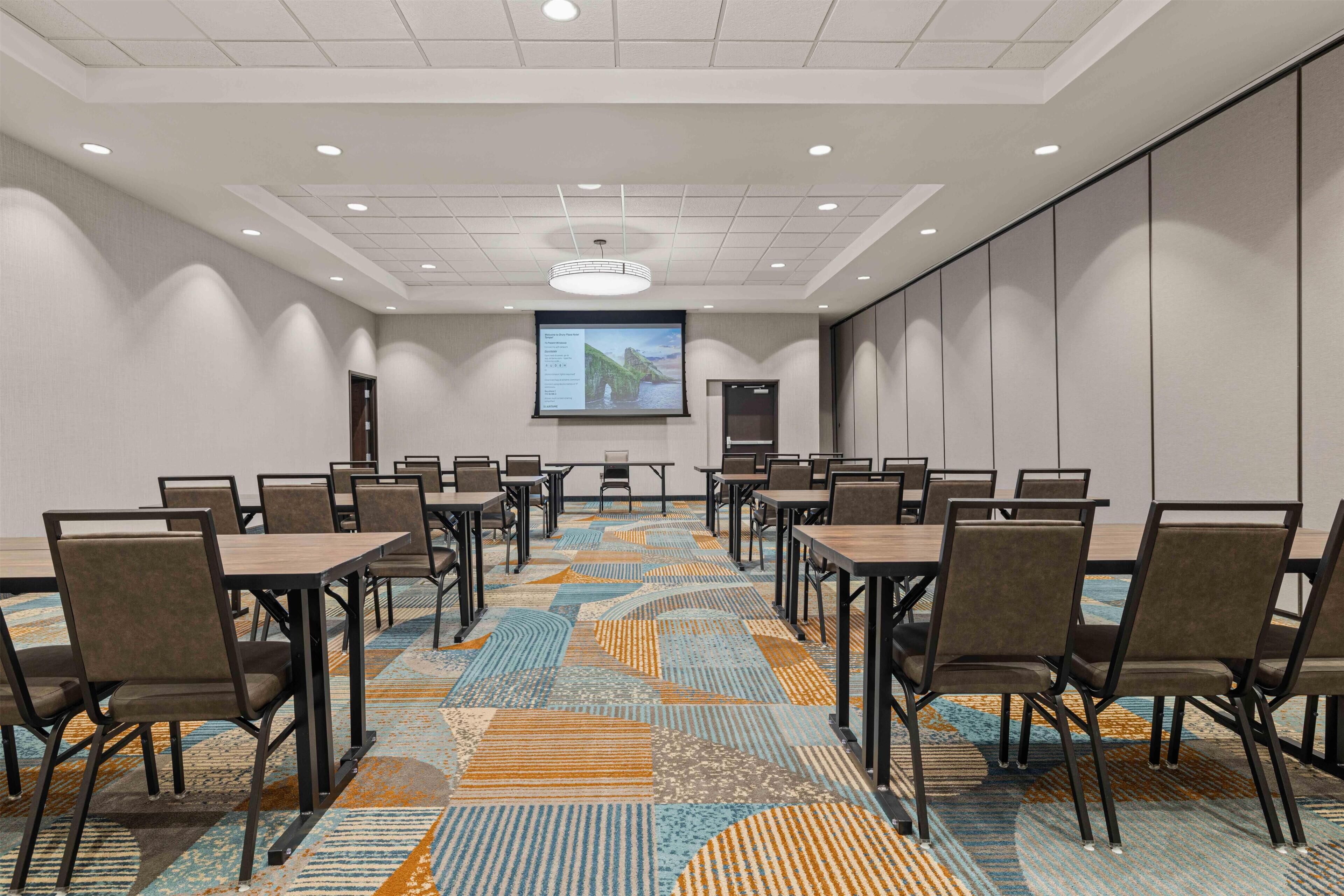 A conference room with a projector screen, multiple tables, and chairs arranged for meetings.