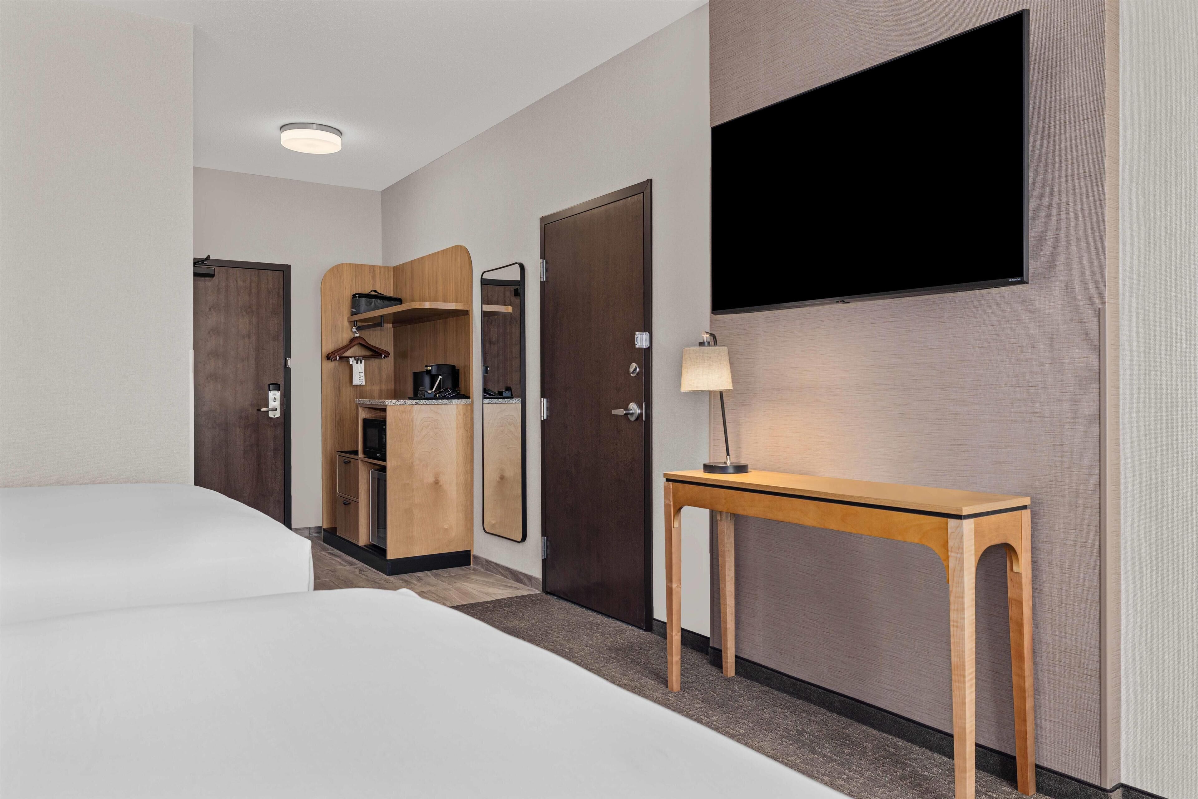 Habitación de hotel con cama, un armario de madera, una mesa con lámpara y televisión montada en la pared.