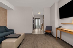 A modern hotel room with a sofa, a small table, a TV mounted on the wall, and a wooden side table. - Drury Plaza Hotel Tampa Brandon (Tampa)