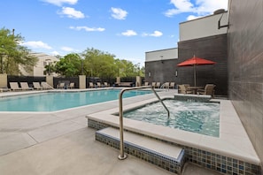 A swimming pool with lounge chairs and a hot tub area, surrounded by a modern building with tiled walls. - Drury Plaza Hotel Tampa Brandon (Tampa)