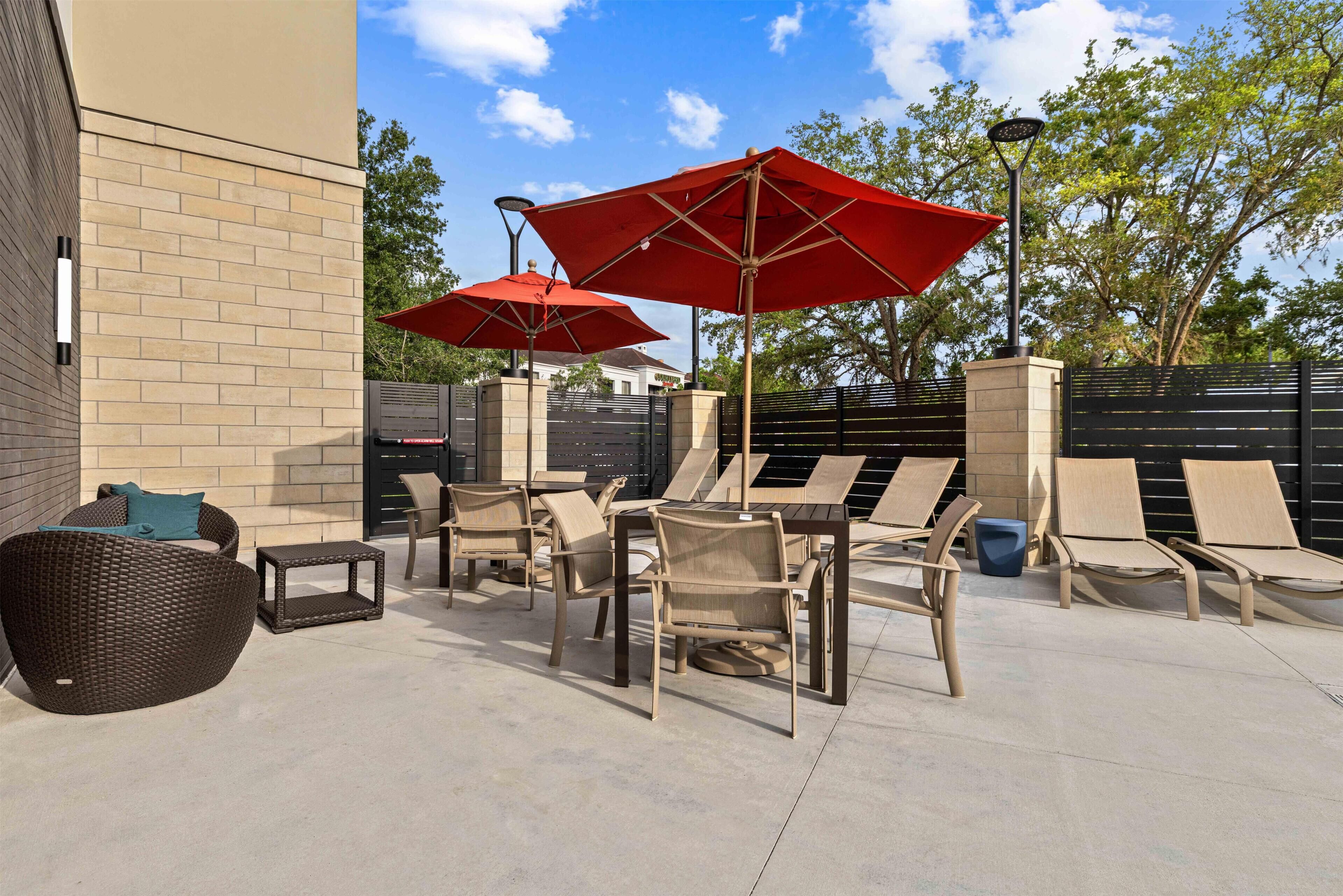Un patio con mobiliario exterior, incluyendo sillas y una mesa, y dos sombrillas rojas.
