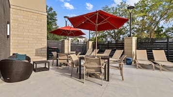 A patio area with outdoor furniture, including chairs and a table, and two red umbrellas.