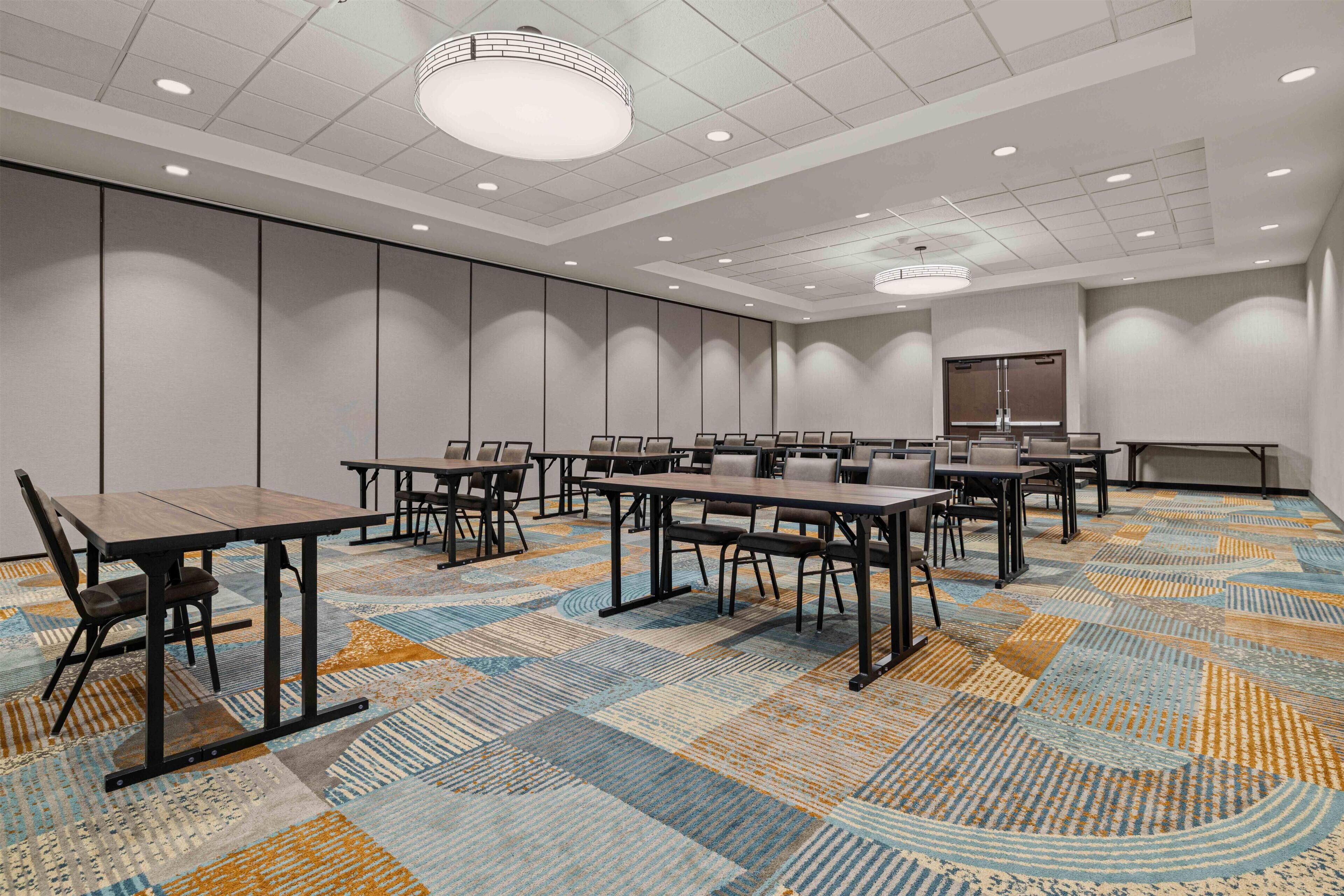Une salle de conférence équipée de plusieurs tables et chaises, d’un grand écran et d’une moquette à motifs.
