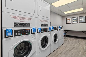 A laundry facility with multiple washing machines, control panels, and a wall-mounted sign. - Drury Plaza Hotel Tampa Brandon (Tampa)