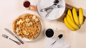 A breakfast setting with waffles, bananas, syrup, coffee, and cutlery on a wooden table.