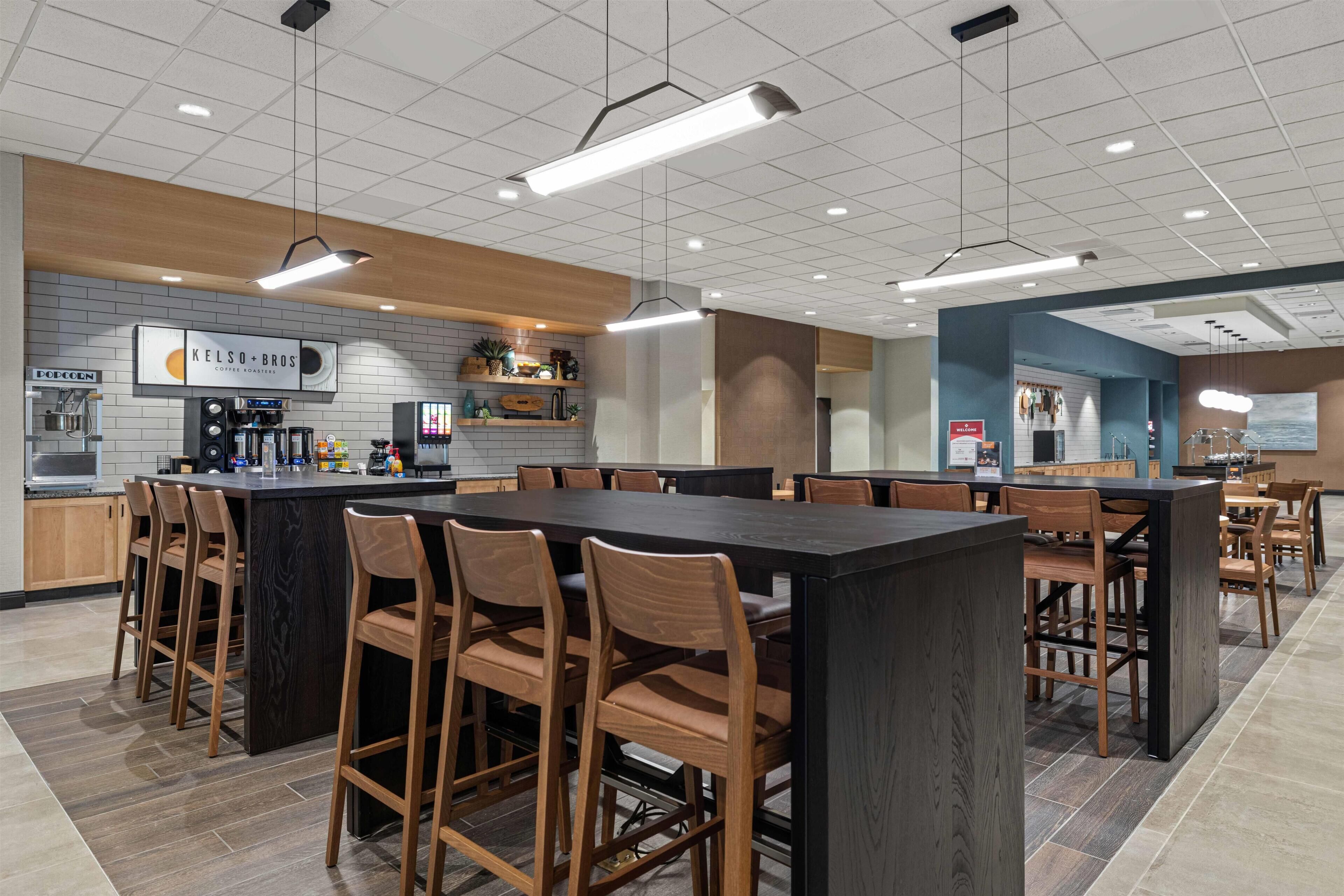A modern cafe with a central island, wooden chairs, and a tiled floor.
